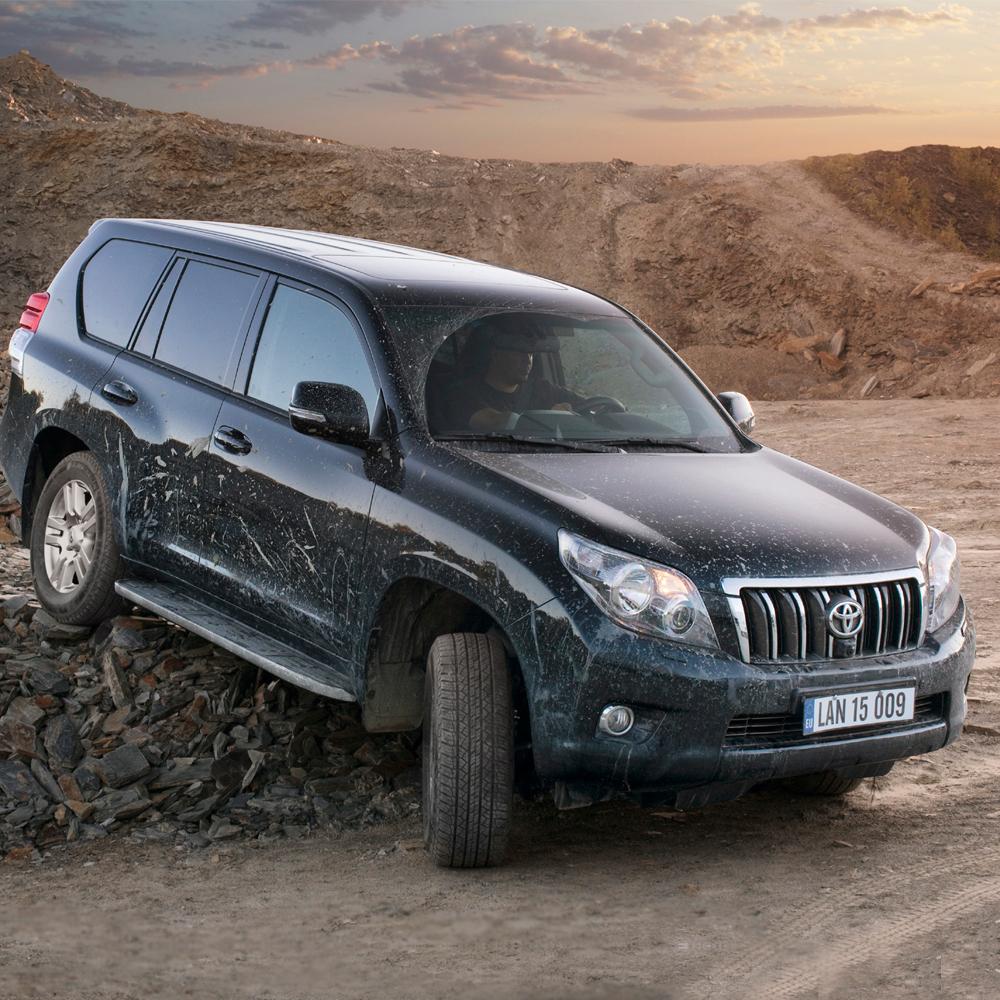 The Old Man Emu Front Trim Packer Fitting Kit OME95PF5 for Toyota Land Cruiser 200 Series, Land Cruiser 120 Series, Land Cruiser 150 Series, equipped with the KDSS (Kinetic Dynamic Suspension System), is parked on a dirt road.