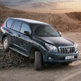 The Old Man Emu Front Trim Packer Fitting Kit OME95PF5 for Toyota Land Cruiser 200 Series, Land Cruiser 120 Series, Land Cruiser 150 Series, equipped with the KDSS (Kinetic Dynamic Suspension System), is parked on a dirt road.