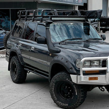 Load image into Gallery viewer, A high-quality ARB Steel Rack with Mesh Floor Kit 70&quot; X 44&quot; for Toyota Land Cruiser parked in front of a building, equipped with roof racks for increased load capacity.