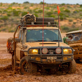Two ARB equipped with fitting kits are driving through mud in a desert.
