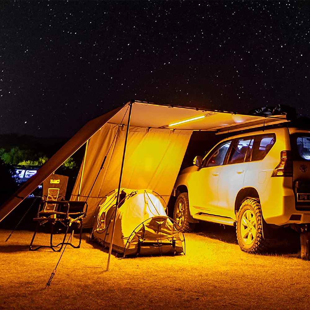 A waterproof SUV is parked under an ARB Touring Awning with Light 814409 at night.
