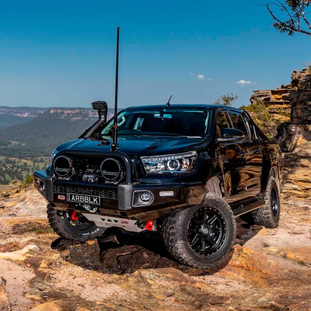 A black Old Man Emu Toyota Hilux parked on a rocky cliff, utilizing the ARB Old Man Emu Rear Nitrocharger Sport 60086 for Toyota Prado 150 Series SWB (Coil Spring Models Only) for optimal performance.