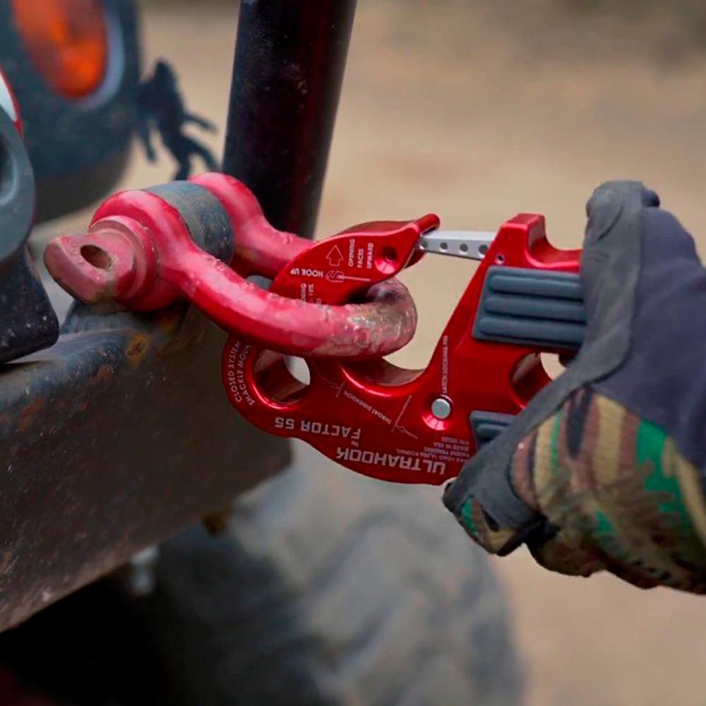 A person holding a Factor 55 UltraHook Winch Shackle Aluminum in Red 00250-01 with ultimate strength to the back of a jeep.