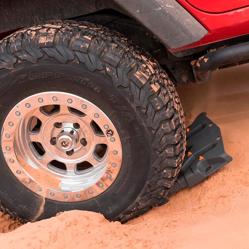 A red jeep with a tire stuck in the sand gets rescued thanks to Aqua ARB Recovery Boards, also known as TRED HD, perfect for off-roading enthusiasts.