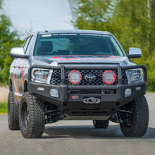 Load image into Gallery viewer, A Toyota Tacoma with Old Man Emu BP-51 2.5 - 3 inch Lift Kit for Tundra (07-21) shock absorbers is driving down a country road, showcasing its off-road performance capabilities with adjustable damping for enhanced control.