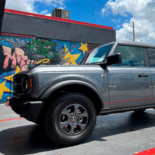 Load image into Gallery viewer, A gray Ford Bronco parked in front of a graffiti wall with an installation vibe, equipped with Old Man Emu ARB Front Coil Springs 3198 for Bronco Base, Big Bend, Outer Banks, Wildtrack (2021-2022) - Light Loads Estimated Lift.