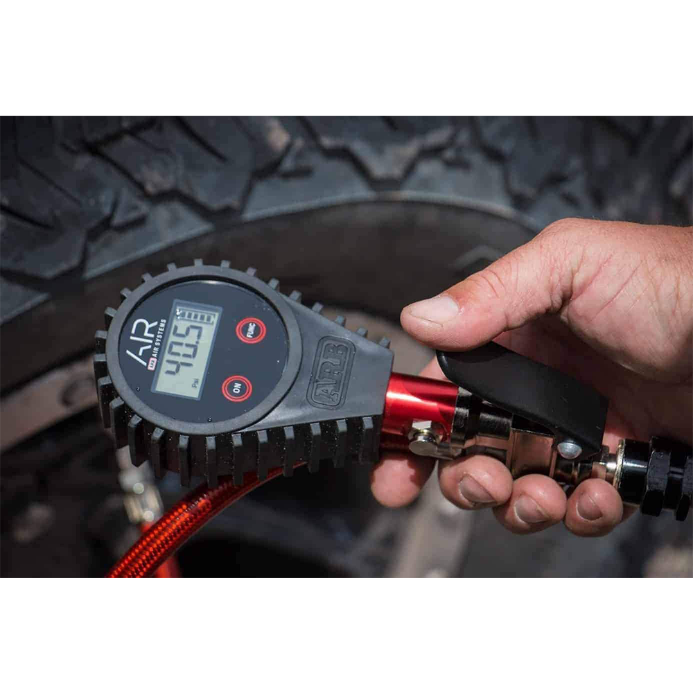 A person holding an ARB Digital Tire Pressure Gauge with Braided Hose ARB601 in front of a tire, ensuring accuracy.