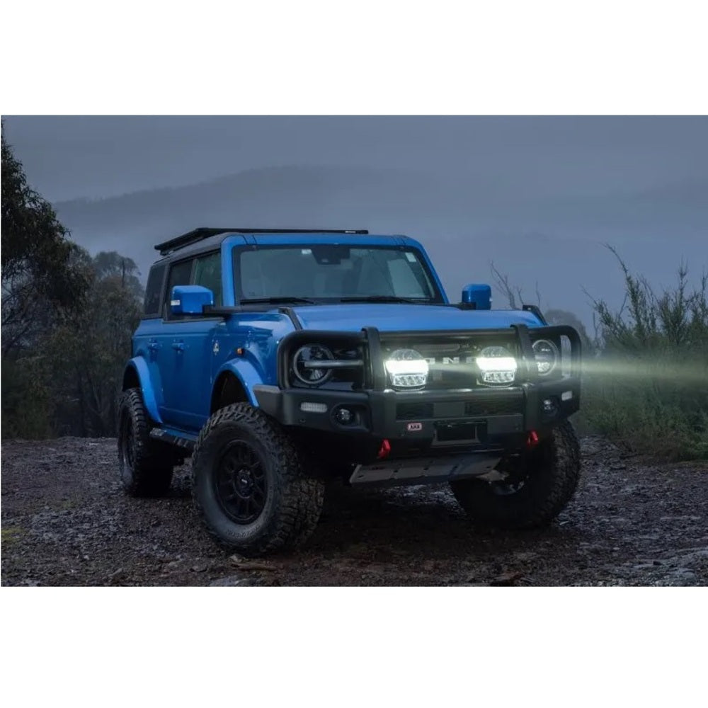 The blue Ford Bronco is parked on a dirt road, beneath the bright glow of ARB Intensity IQ LED Driving Lights ARBVX17.