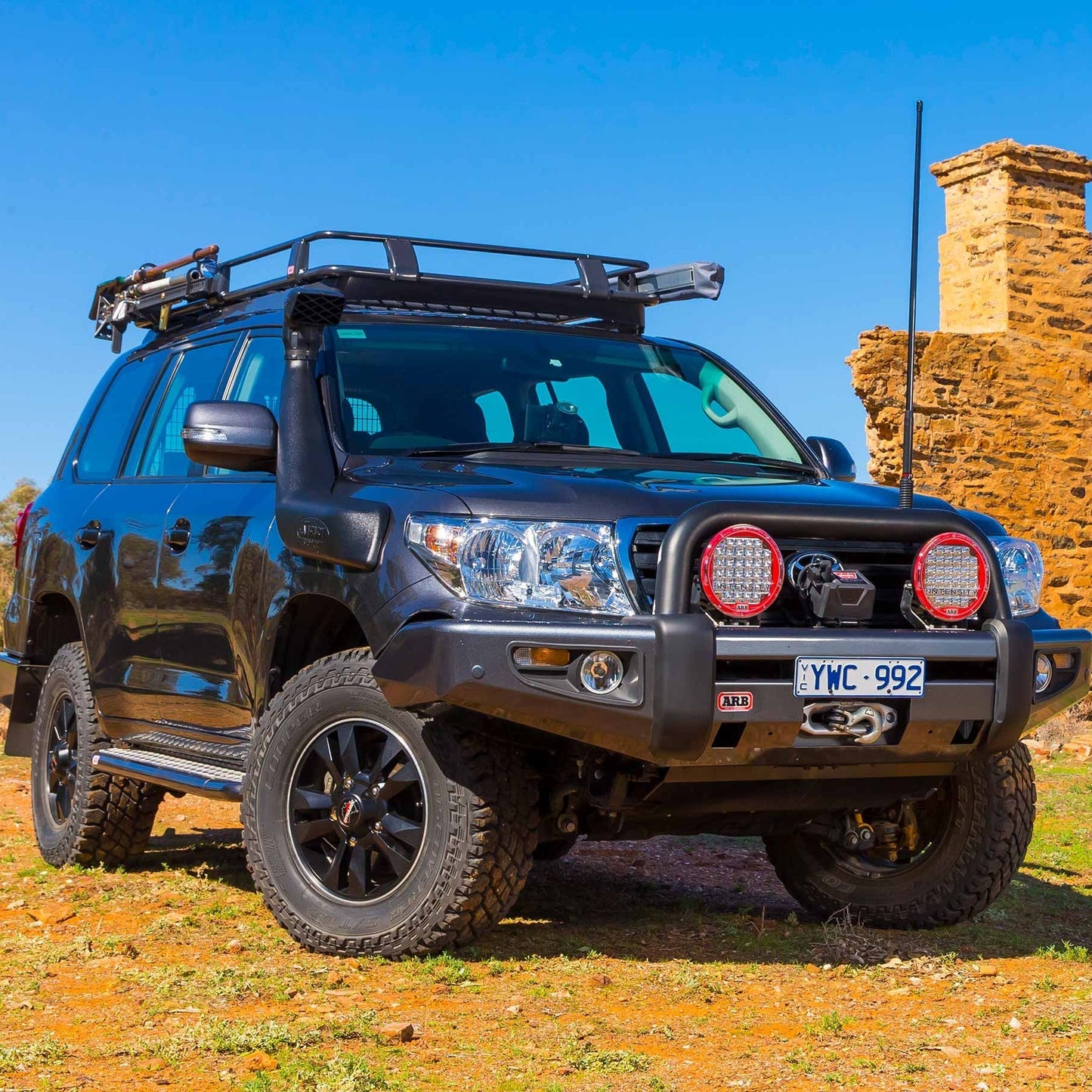 A black Toyota Land Cruiser with off-road performance capability, equipped with King Shocks and a strong suspension system, parked on a dirt road.