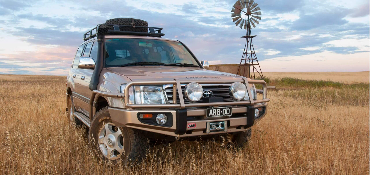 A Toyota Land Cruiser parked in a field with a windmill showcasing the versatile BASE Rack and its dovetail system, secured with ARB Eye Bolt Tie-Downs.