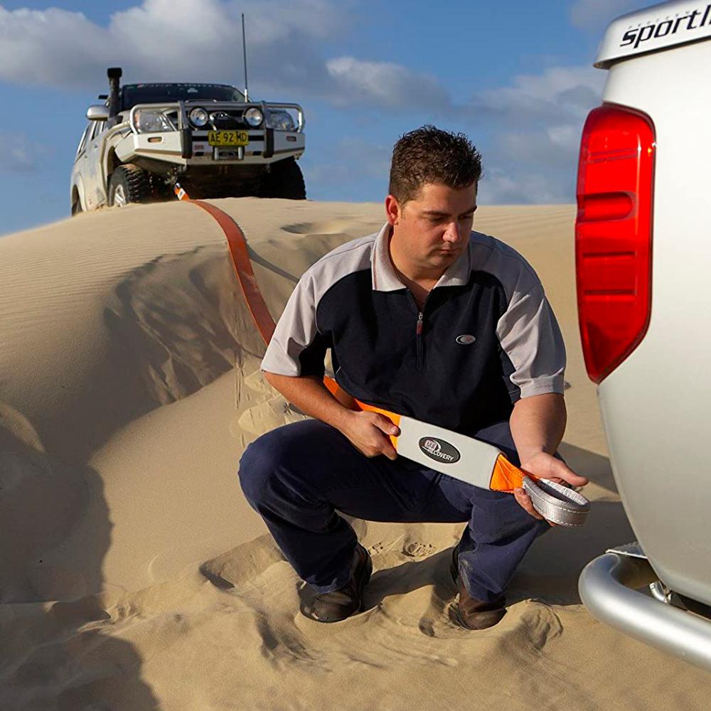 A man performing vehicle recovery in front of a truck stuck on a sand dune, using an ARB715LB Snatch Block Strap from ARB.