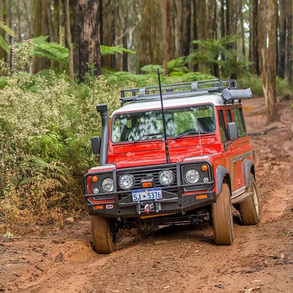 A red ARB RD196 Air Locker Differential Nissan C200K with 31 Splines, known for its effective design, is confidently driving down a dirt road, showcasing its traction and ensuring the comfort and safety of its occupants.