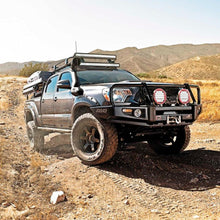 Load image into Gallery viewer, A black Toyota Tacoma with the Old Man Emu ARB Rear Nitrocharger Sport Shock Absorber 60091 is driving down a dirt road.