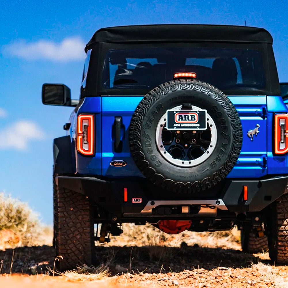 The rear end of a blue jeep on a dirt road, showcasing its Old Man Emu Front Stabilizer Bar Kit OMESTAB10 for Ford Bronco suspension system from Old Man Emu for enhanced ride quality and increased load-carrying capacity.