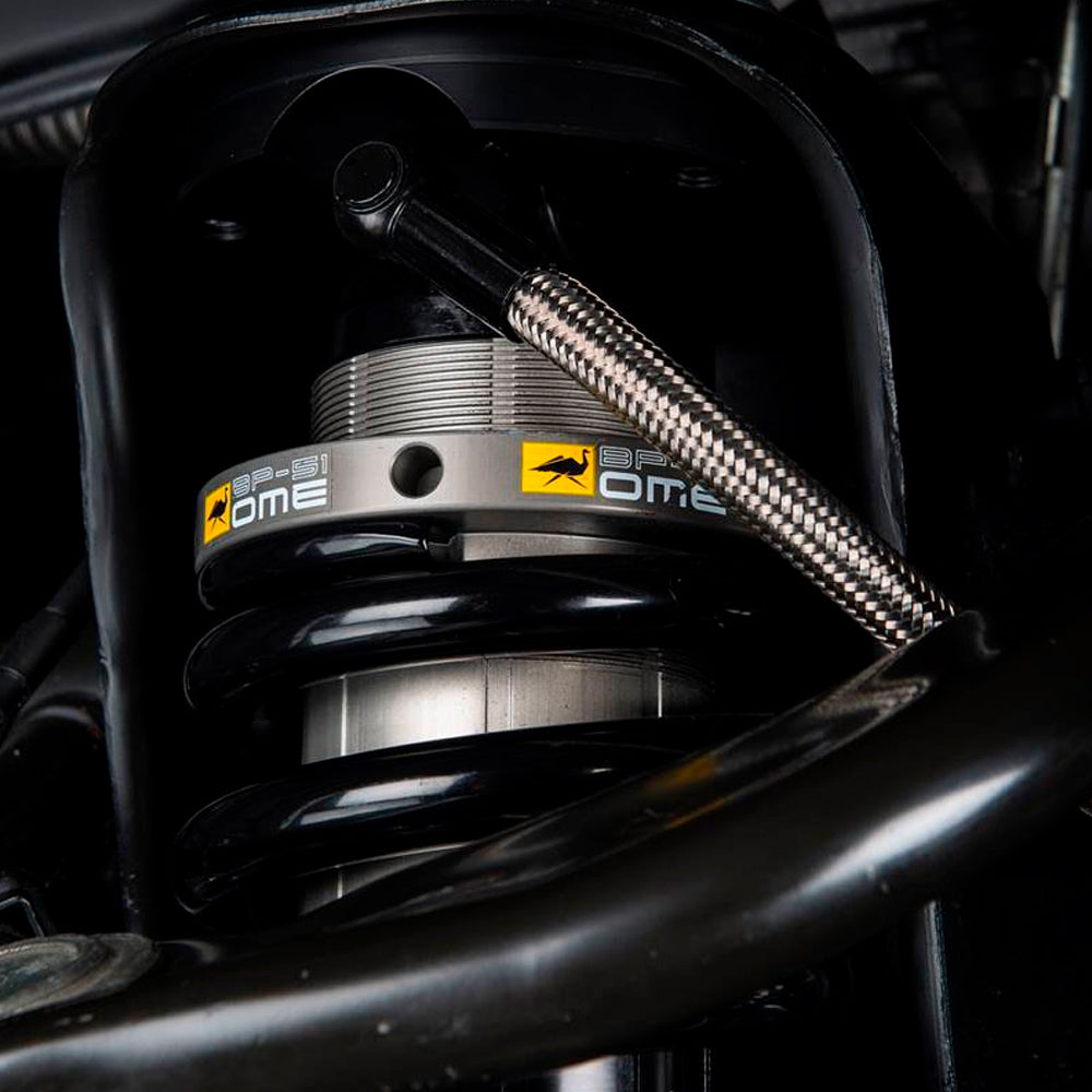 A close up of a Old Man Emu motorcycle suspension system featuring a shock absorber body and a remote reservoir connected by a high-temperature hose.