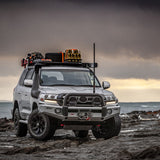 An ARB Base Rack Mount Kit for Toyota Land Cruiser 200 Series (2008-2022) ARB 17915010, equipped with a dovetail mounting system, is parked on a rocky beach.