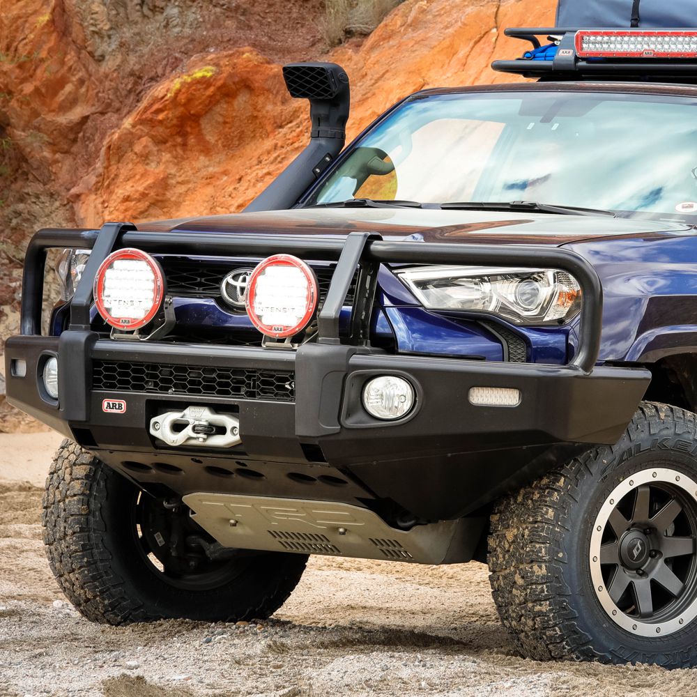On a dirt road, a blue Toyota 4Runner is parked with the help of an ARB Base Rack Deflector For Toyota 4Runner (2010-2022) ARB 17921040.