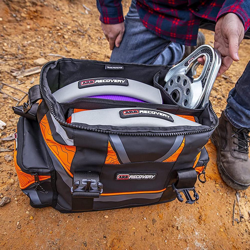 A man is holding an ARB bag full of ARB Premium Recovery Kit + Recovery Bag + Leather back gloves and more RK9A, specifically designed for small SUVs, containing a recovery kit tailored to the vehicle's weight.