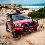 An Old Man Emu red Toyota Tacoma with ARB Old Man Emu Rear Coil Springs 2896 for Prado150 Series, FJ Cruiser, 4Runner - Constant Load 440 lbs. is driving through the sand on the beach, showcasing its ride height and easy installation.