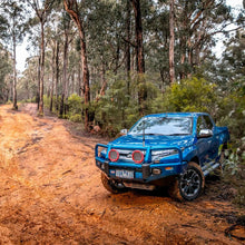 Load image into Gallery viewer, A blue truck with Old Man Emu Front Nitrocharger Sport Shock Absorber 90004 for Toyota Tacoma V6 &amp; 4 Cylinder (1998 - 2004) / 4Runner 1996 - 2002 driving down a dirt road in the woods.