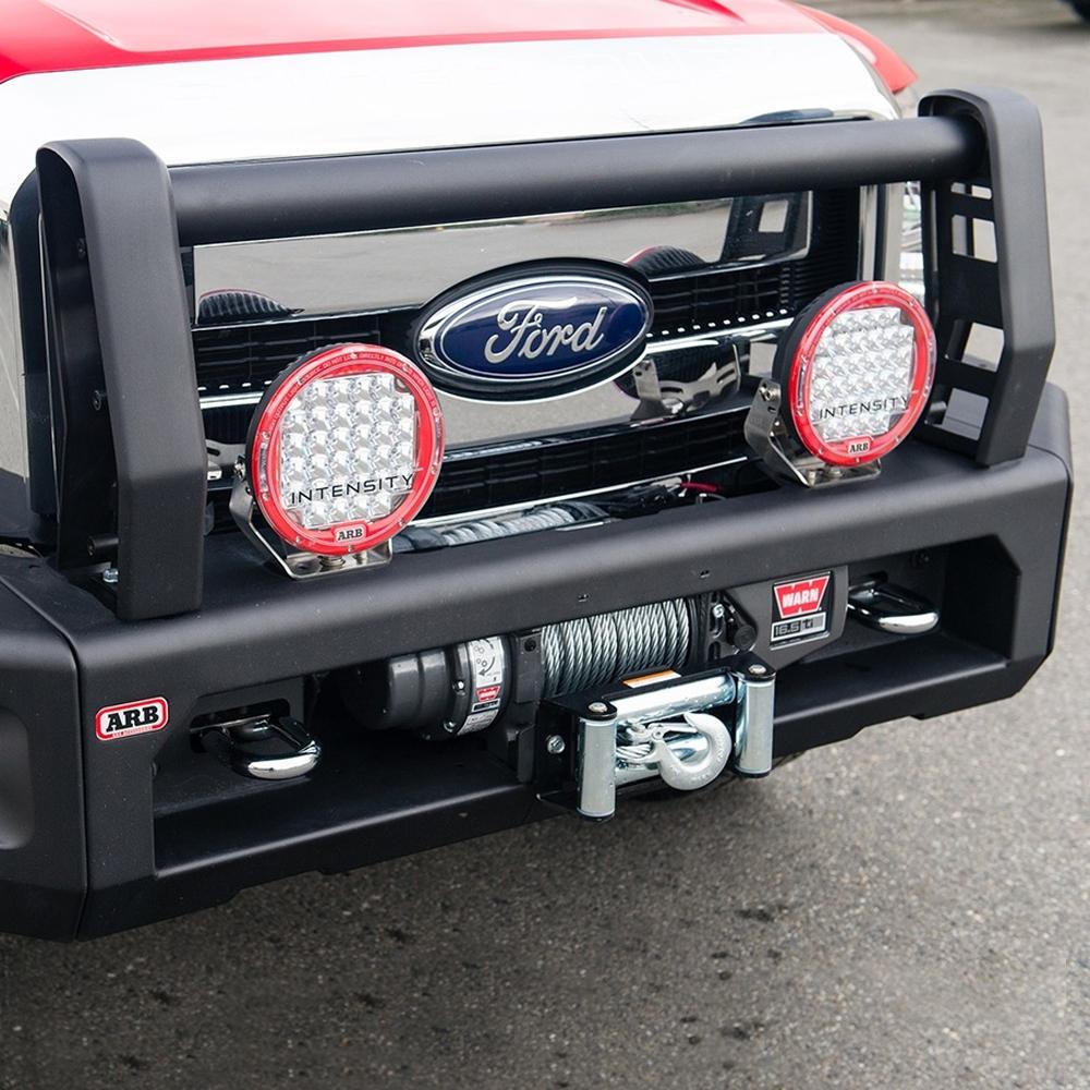A red Ford F-250 pickup truck with a Sahara Style Modular Winch Bumper Kit ARB 2236020 by ARB, which has secure mounting points for an electric winch provision and a light bar on the front bumper.