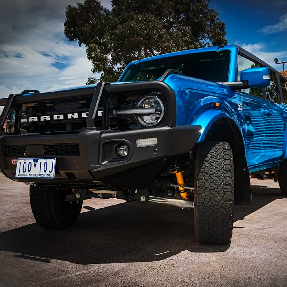 An Old Man Emu blue Ford Bronco with an ARB Trim Packer Kit FK111 (21-ON) suspension system parked in a parking lot.