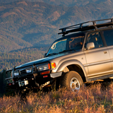 An Old Man Emu Toyota Land Cruiser parked in a grassy field, showcasing its impressive ride height increase and the reliable installation of ARB Old Man Emu Rear Coil Springs 3049.