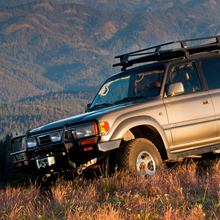 Load image into Gallery viewer, An Old Man Emu Toyota Land Cruiser, equipped with Old Man Emu Front Coil Springs 2419 for Toyota Landcruiser 80 and 105 Series (3.5 inch LIFT - Constant Load 110.231 LB) for optimal suspension, stylishly parked in a lush grassy field. The Land Cruiser&#39;s design ensures easy installation of additional accessories or modifications. With