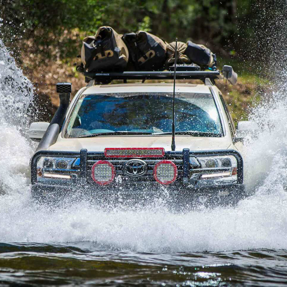 The ARB Safari Snorkel Intake Kit Toyota 4Runner 2003-2009 4.7L V8 SS440HF, equipped with a durable material, is driving through the water with its vehicle-specific modifications.