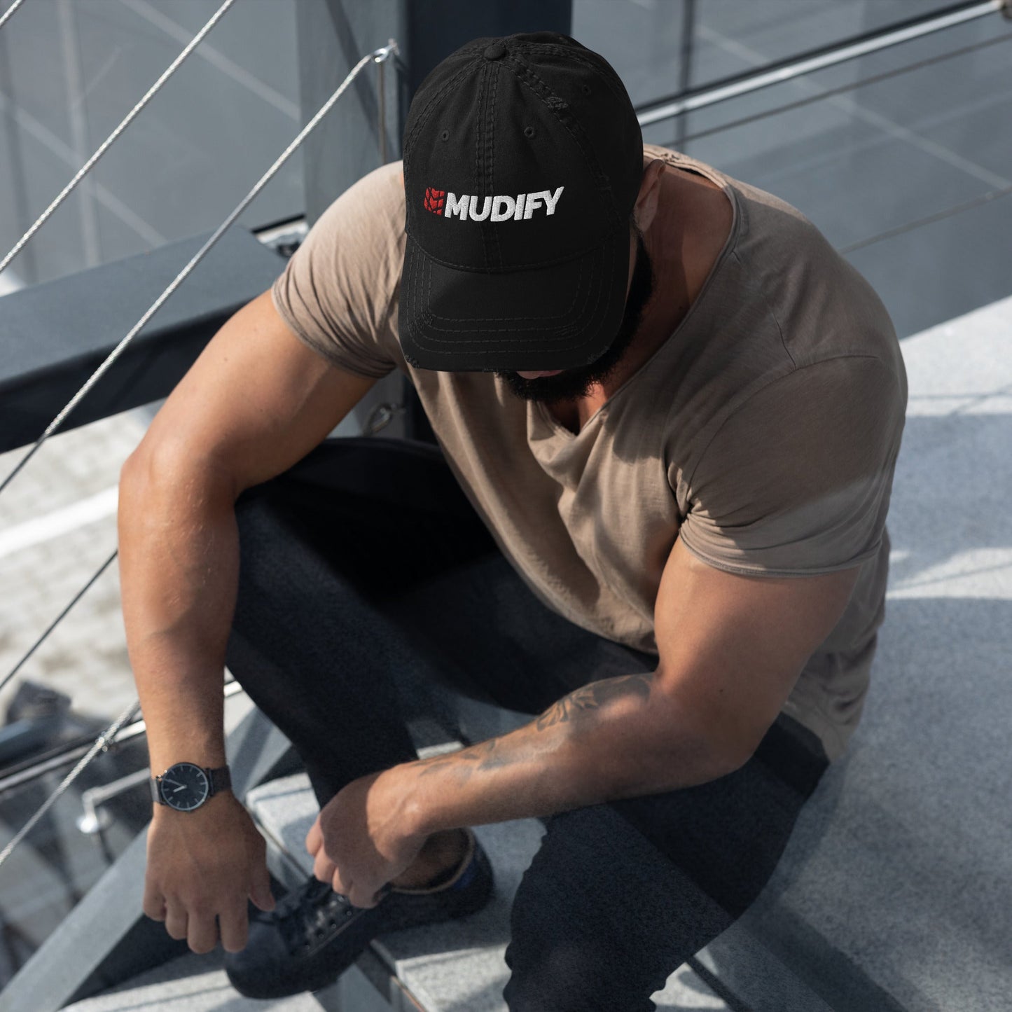A fashionable man sitting on a stairway wearing a Mudify Basic Mudify Cap.