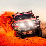 A red Old Man Emu Toyota Tacoma with increased ride height is driving through the desert.