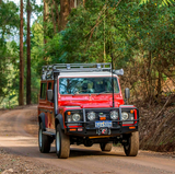 A red Old Man Emu Land Rover with increased ride height is driving down a dirt road.
