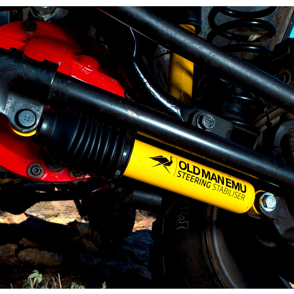 A close up of a yellow and black Old Man Emu Steering Stabilizer OMESD48 suspension with steering stabilizers on a motorcycle.