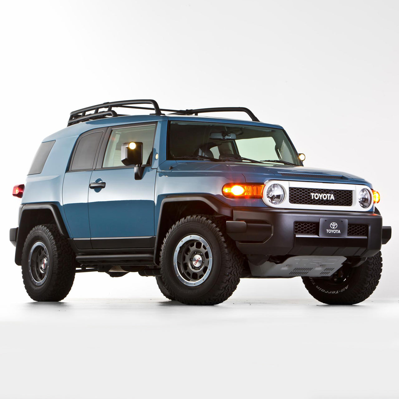 A blue Toyota FJ Cruiser is shown in a studio with upgraded suspension featuring Old Man Emu BP-51 shock absorbers.