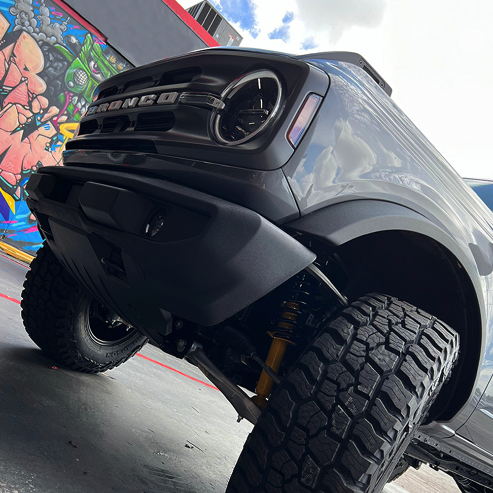 The front end of a black truck with graffiti on it featuring a unique ride height and custom suspension, equipped with the ARB Trim Packer Kit FK111 for Ford Bronco (21-ON) by Old Man Emu.