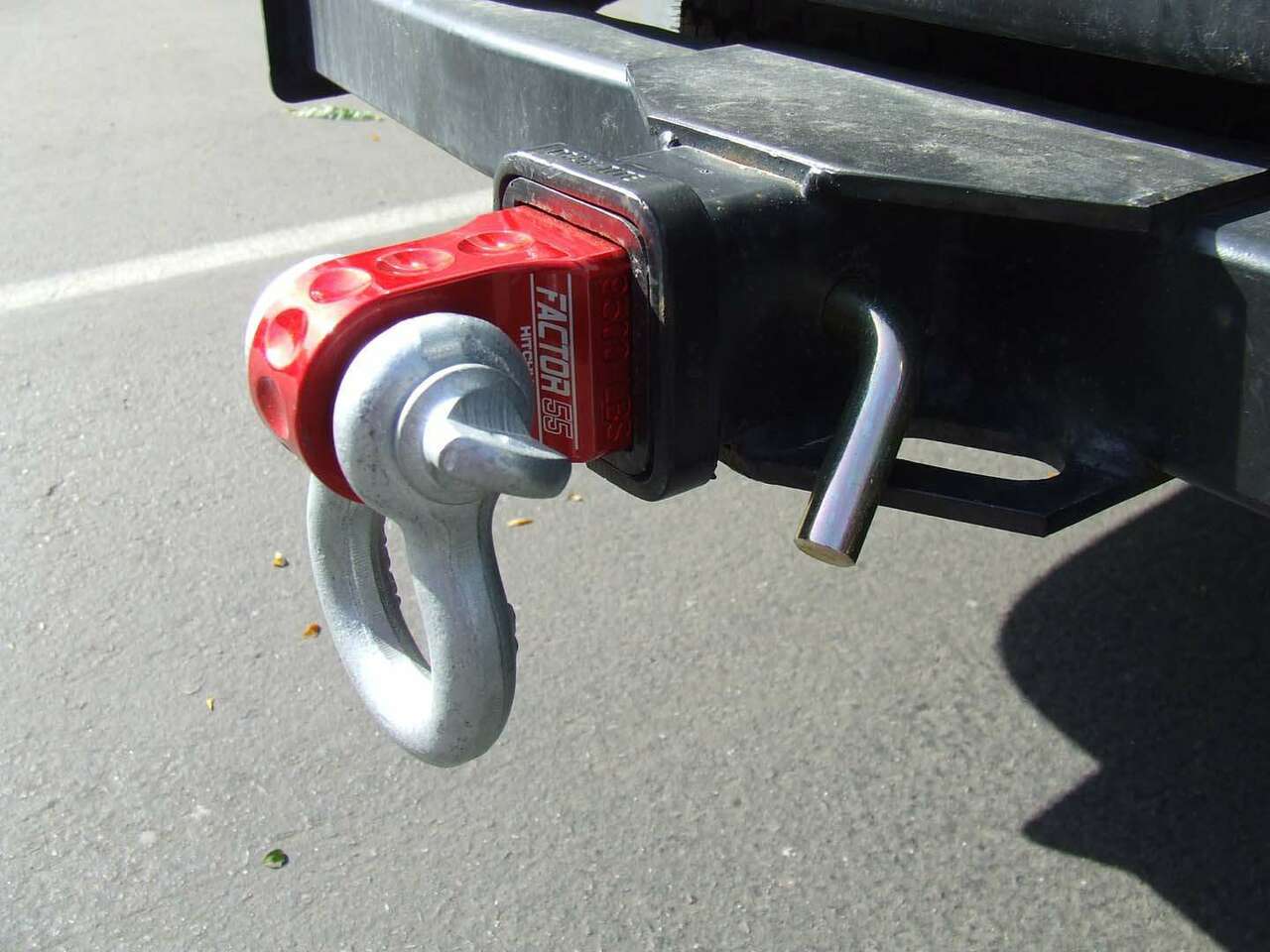 A red truck with a Factor 55 HitchLink 2.0in 00020-04, featuring an aluminum hitchlink and powder coated finish, is equipped with a hook attached to its back.