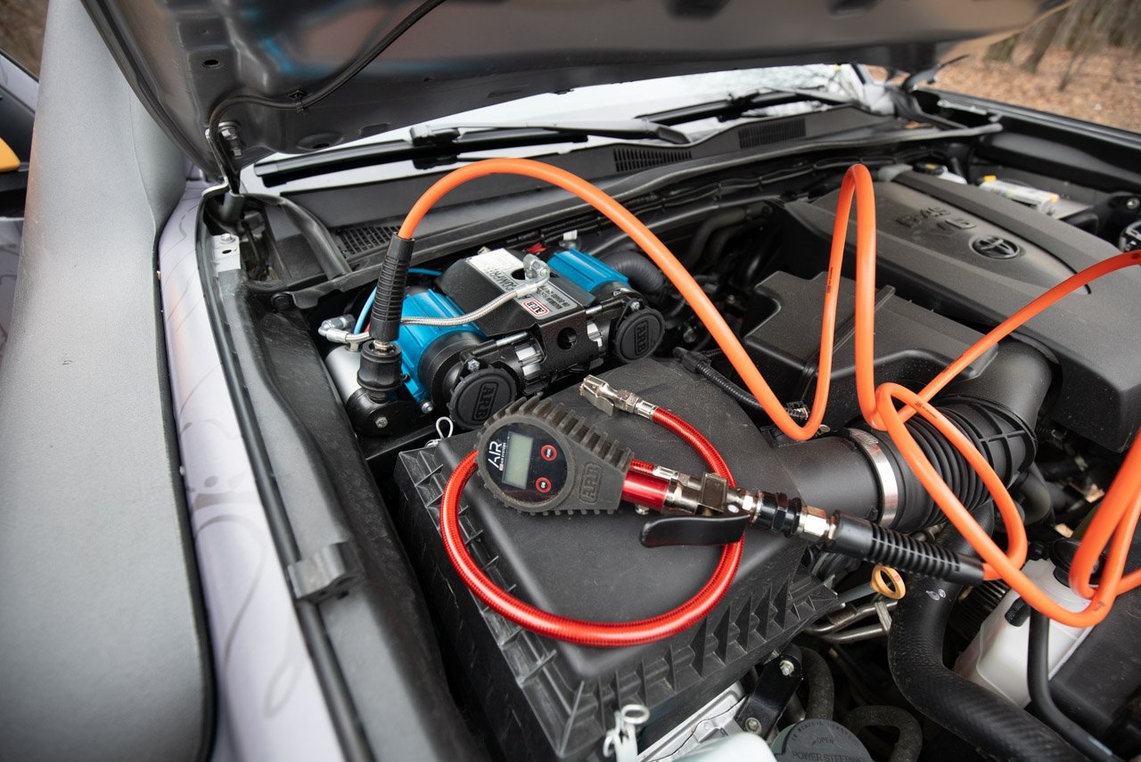 A car with a CKMTA12 Bundle Kit - ARB Inflation Kit, Air Compressor and Digital Tire inflator and hoses in the hood.