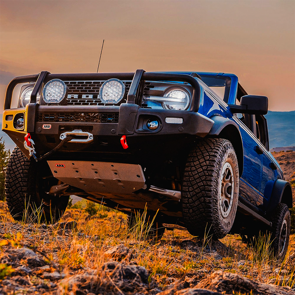 A blue Nissan B-series truck with a high load-carrying capacity is parked in a rocky area, equipped with ARB Old Man Emu Front Stabilizer Bar Kit OMESTAB10 for Ford Bronco suspension systems for enhanced ride quality.