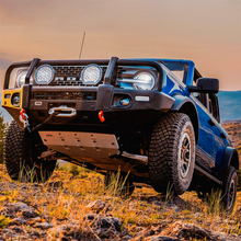 Load image into Gallery viewer, A blue Nissan B-series truck with a high load-carrying capacity is parked in a rocky area, equipped with ARB Old Man Emu Front Stabilizer Bar Kit OMESTAB10 for Ford Bronco suspension systems for enhanced ride quality.