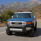 A blue Toyota FJ Cruiser with Old Man Emu BP-51 2.5 - 3 inch Lift Kit for FJ Cruiser (10-ON) shock absorbers is driving down a mountain road.