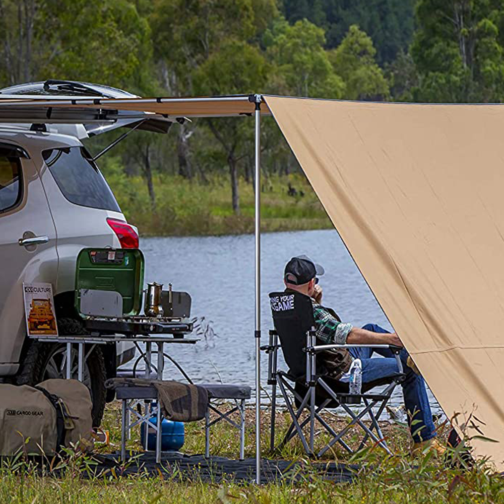 A man sits in a chair next to a shady area near a lake under the ARB Touring Awning with Light 814409 by ARB.