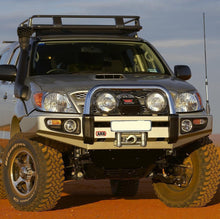 Load image into Gallery viewer, A silver Toyota Tacoma is parked on a dirt road, showcasing its impressive Old Man Emu Front Nitrocharger Sport Shock 90011 performance.