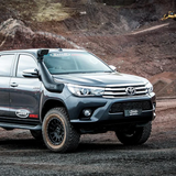 The Safari Snorkel Intake Kit SS123HP for Toyota Hilux (2015-2022), equipped with a Turbo Diesel engine, is parked on a dirt road.