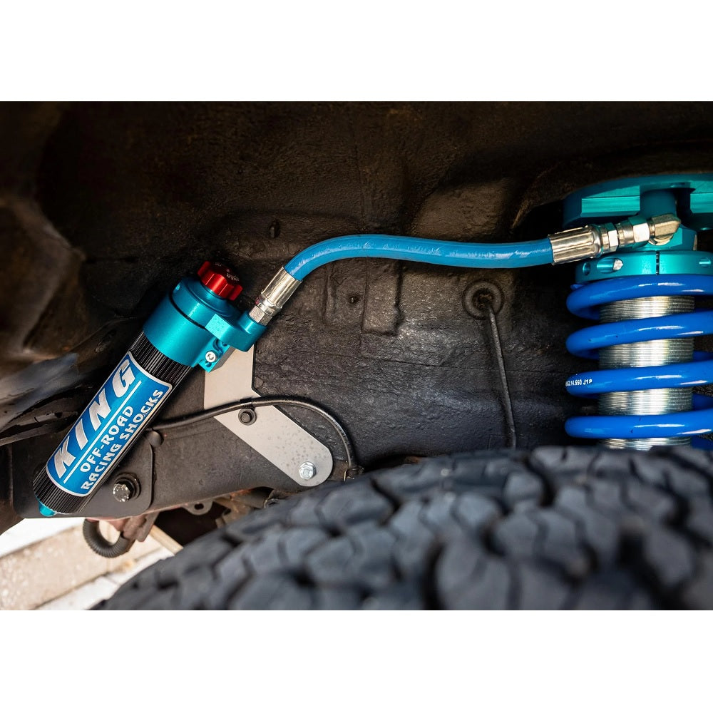 The underside of a vehicle is fitted with a blue King Shocks shock, enhancing stability and off-road performance.