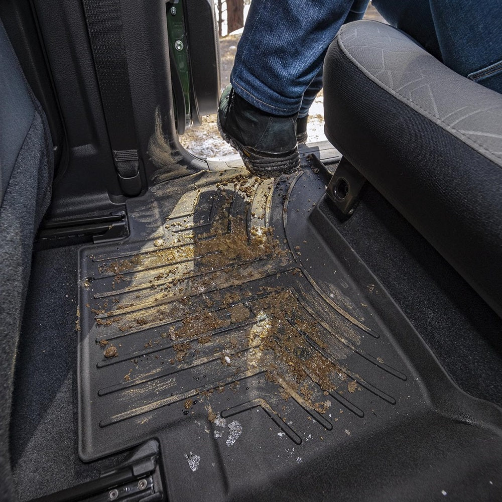 A person is standing in the back seat of a vehicle equipped with Weathertech Floorliner HP 2nd Row Floor Mats, suitable for extreme weather environments.